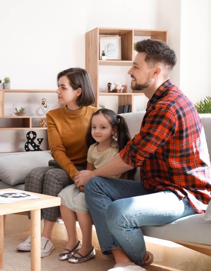 Parents and their child sitting together in a warm living room.