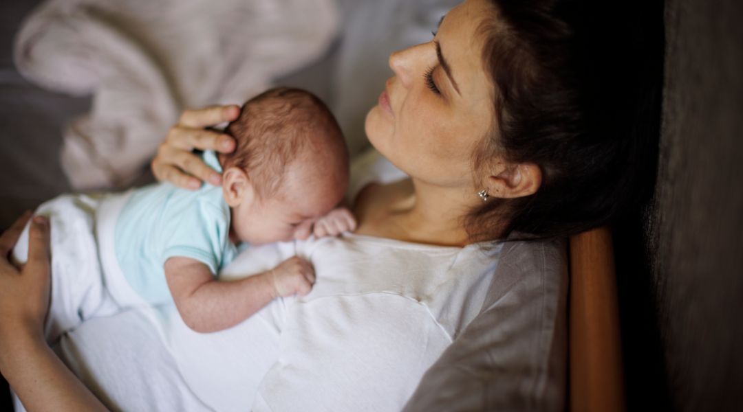 A new parent resting with a sleeping baby on her chest.