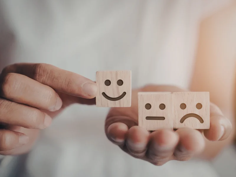 Hands holding wooden blocks showing happy, neutral, and sad expressions.