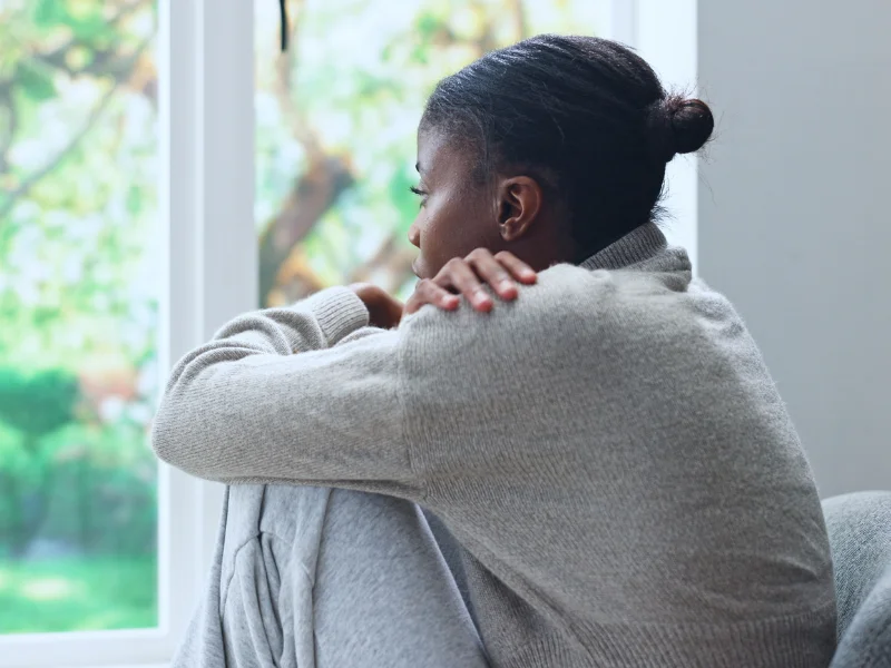 A woman resting her arms on her knees and looking out a window.