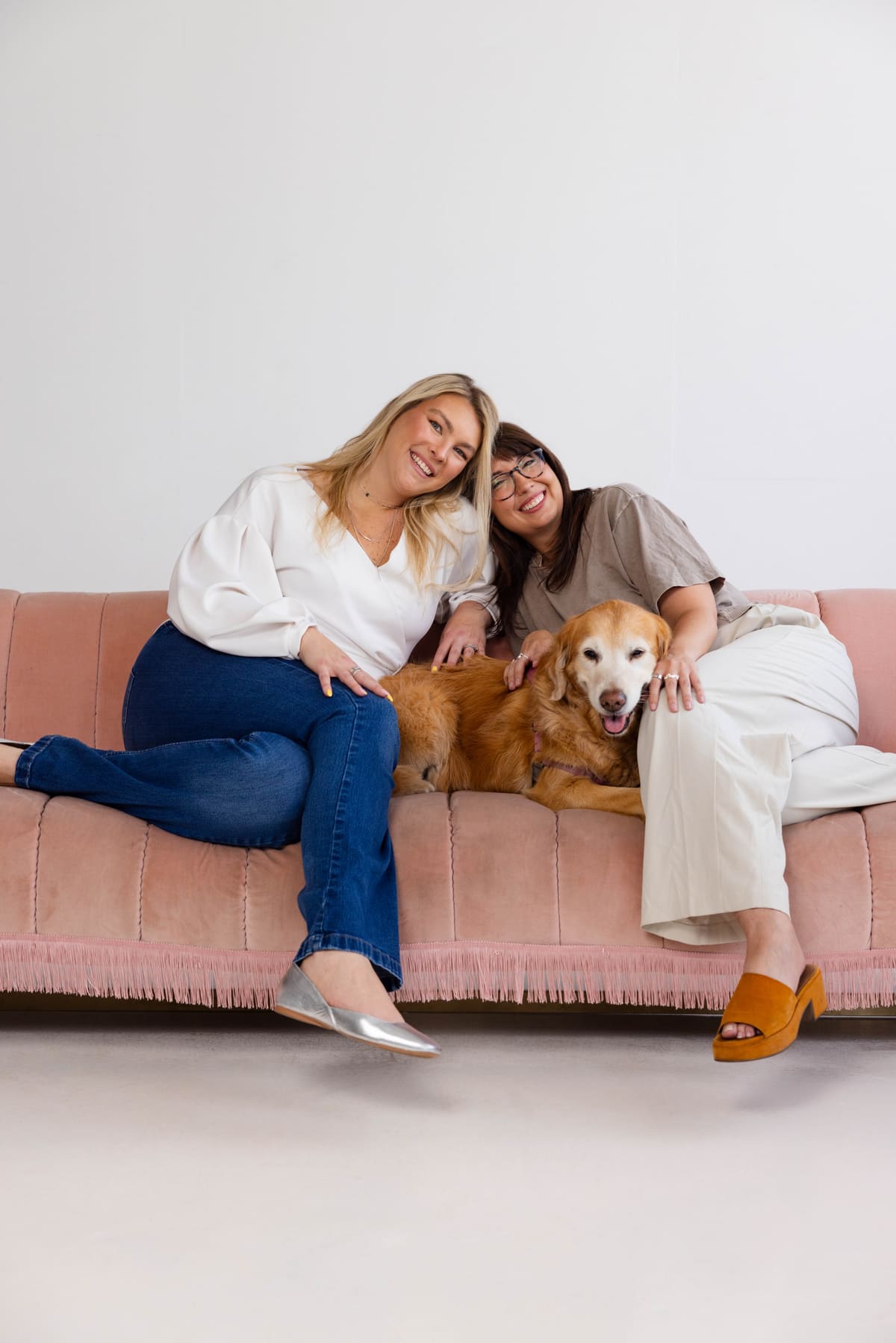 Hannah Snider and Tori Brown relaxing with Lola on a blush sofa.